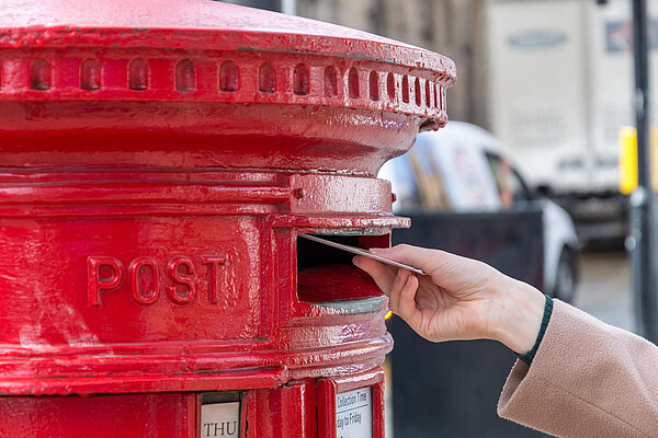 A woman posting a letter into a post box.